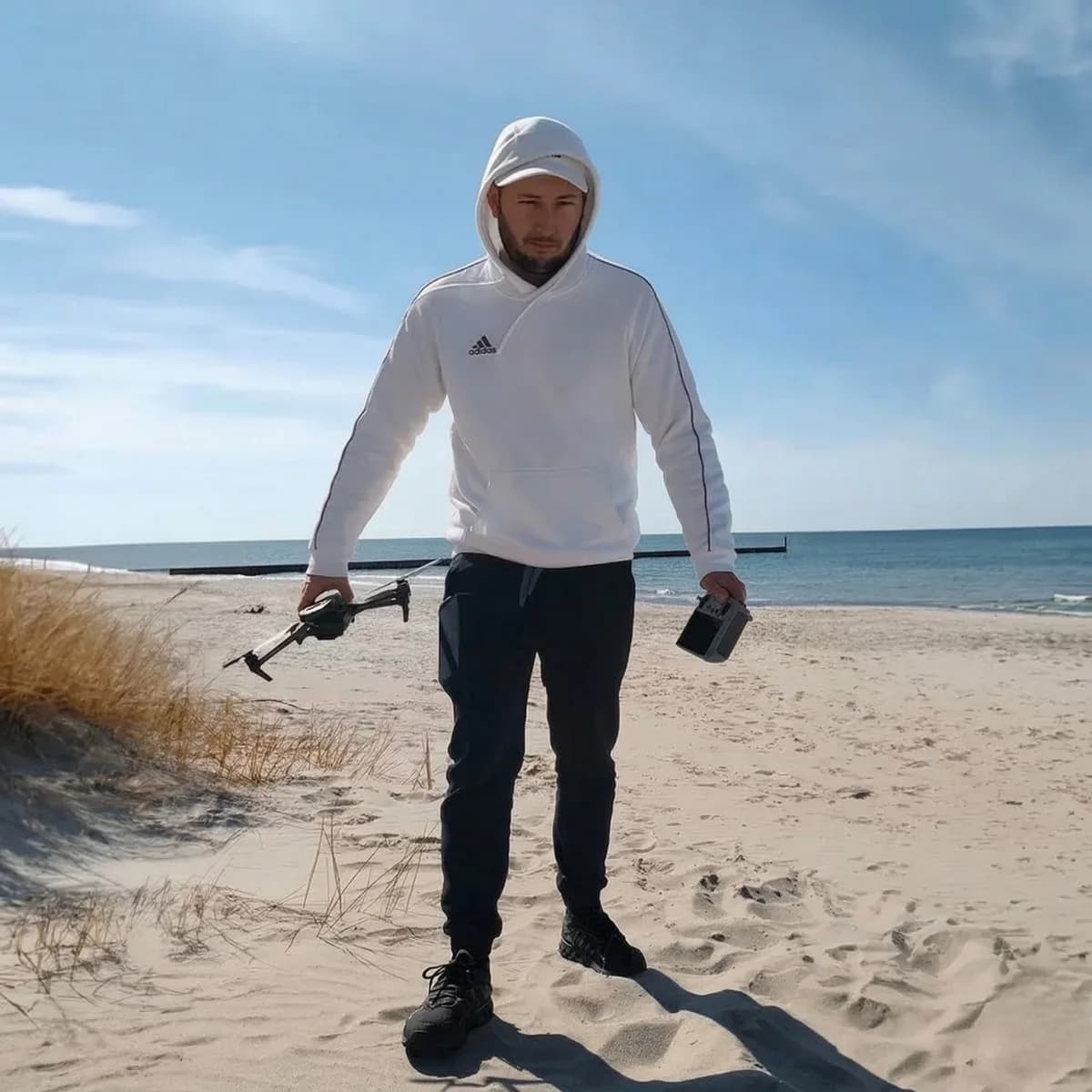 Damian Grygierek z dronem i kontrolerem na plaży nad morzem